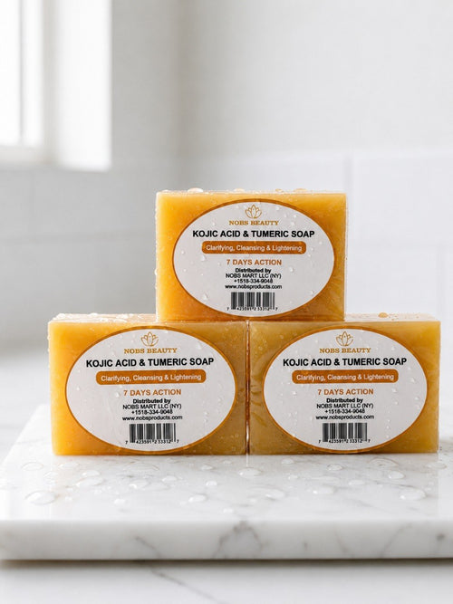 Three rectangular bars of Nourish Beauty Kojic Acid & Turmeric Soap arranged in a pyramid stack on a white marble surface with water droplets, against a bright, softly blurred background.